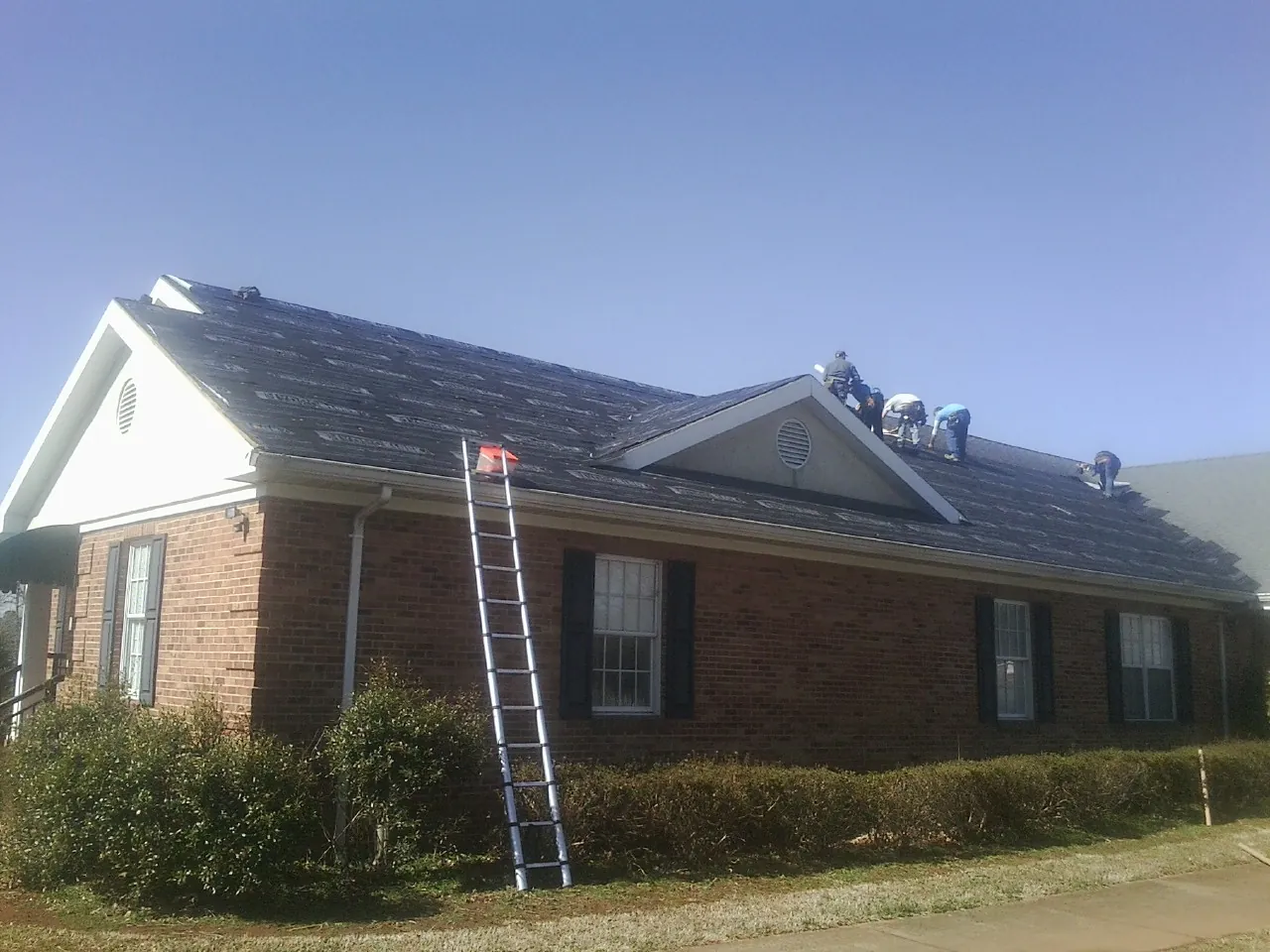 Crew tearing shingles off a brick ranch roof with a ladder set — Emergency Roof Repair work by our crew in Versailles