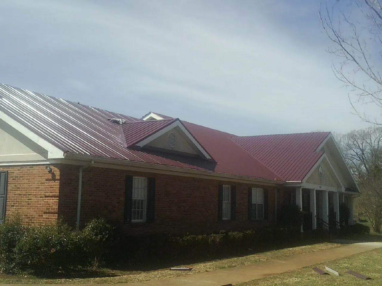 Red metal roof with gabled entries on a long brick building, from a Hail Damage Roof Repair job in Versailles