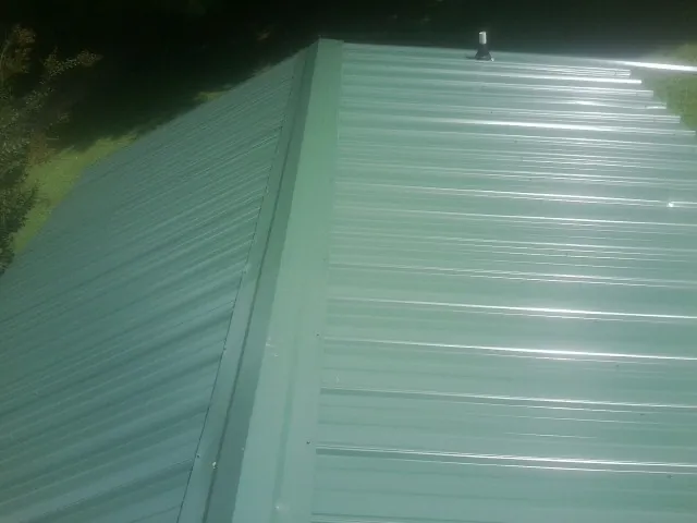 New green metal panels meeting at the ridge of a roof — Flat Roof Repair work by our crew in Versailles